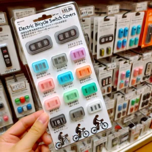 100均で購入できる電動自転車スイッチカバーの種類を並べた商品写真風の画像。透明のシリコンカバー、カラフルなカバー、防水タイプのカバーなどが写っている。背景はシンプルな白色。商品ごとに簡単な説明ラベルがついている。