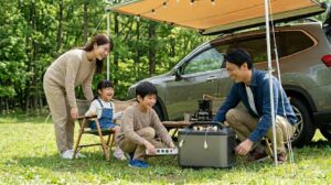 キャンプ場でJVCケンウッド製のポータブル電源を接続する日本人男性。国内メーカーの安心感。