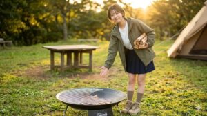 日本人女性キャンパーがファイヤーディスクに小さな網をずらして載せ、薪投入用の開口部を作る工夫。