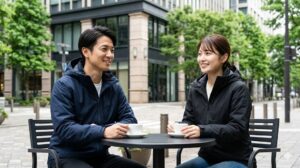 都会的なカフェでヘリーハンセンのミニマルなジャケットを着用してくつろぐ日本人カップル。北欧デザインの洗練を示す。