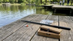 舎人公園のウッドデッキに置かれた、初心者向けののべ竿(小継振出竿)とシンプルな仕掛けセット(竿、糸、ウキ、針、エサ箱)。リールのない釣具。