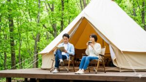 2026年ゴールデンウィークの5連休、混雑を避けて新緑の中でのグランピングを楽しむ日本人カップル。ｍ
