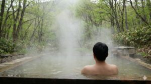 北海道の新緑に囲まれた秘湯で、一人静かに湯に浸かる男性。