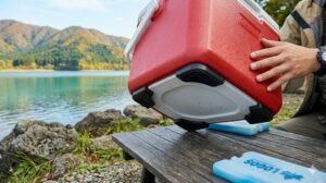木製テーブルの上に置かれたコールマン テイク6クーラーボックスの底面にある4つのプラスチック製の脚が、空気層（クリアランス）を作っている様子。湖畔キャンプ場。